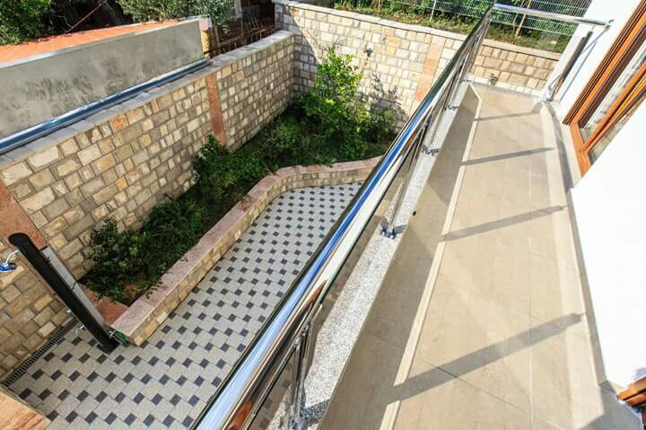 Balkon mit Fliesenbelag und Metallgeländer in einem Haus in Šušanj, Montenegro, Blick auf einen privaten Hof mit Garten.