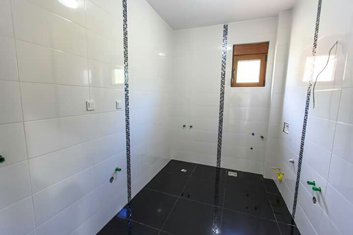 Badezimmer mit Fliesenverkleidung in einem im Bau befindlichen Haus in Šušanj, Montenegro: weiße Wände und schwarzer Boden mit Mosaik.
