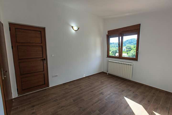 Helles Schlafzimmer in einem Haus in Šušanj, Montenegro: Holztüren, Holzoptik-Boden, Heizkörper und Blick auf grüne Berge.