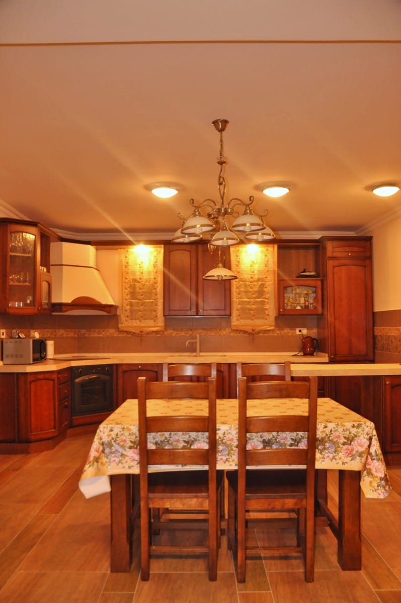 Kitchen with wooden cabinetry and dining area in a villa in Đenovići, Montenegro. Classic interior with lighting.