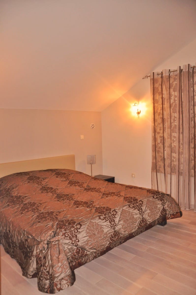 Cozy bedroom with a double bed in a villa in Đenovići, Montenegro: sloped ceiling, light flooring, and curtains.