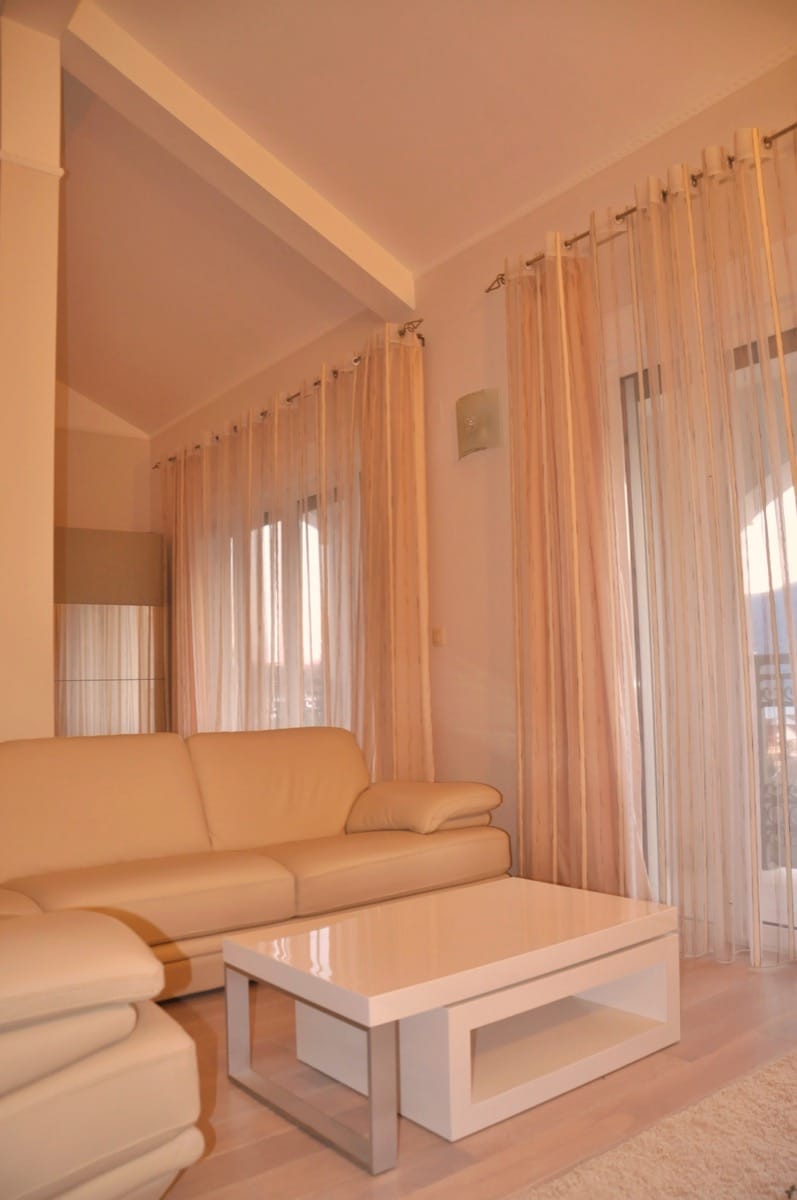 Bright living room with a leather sofa and glossy table in a villa in Đenovići, Montenegro, with panoramic windows.