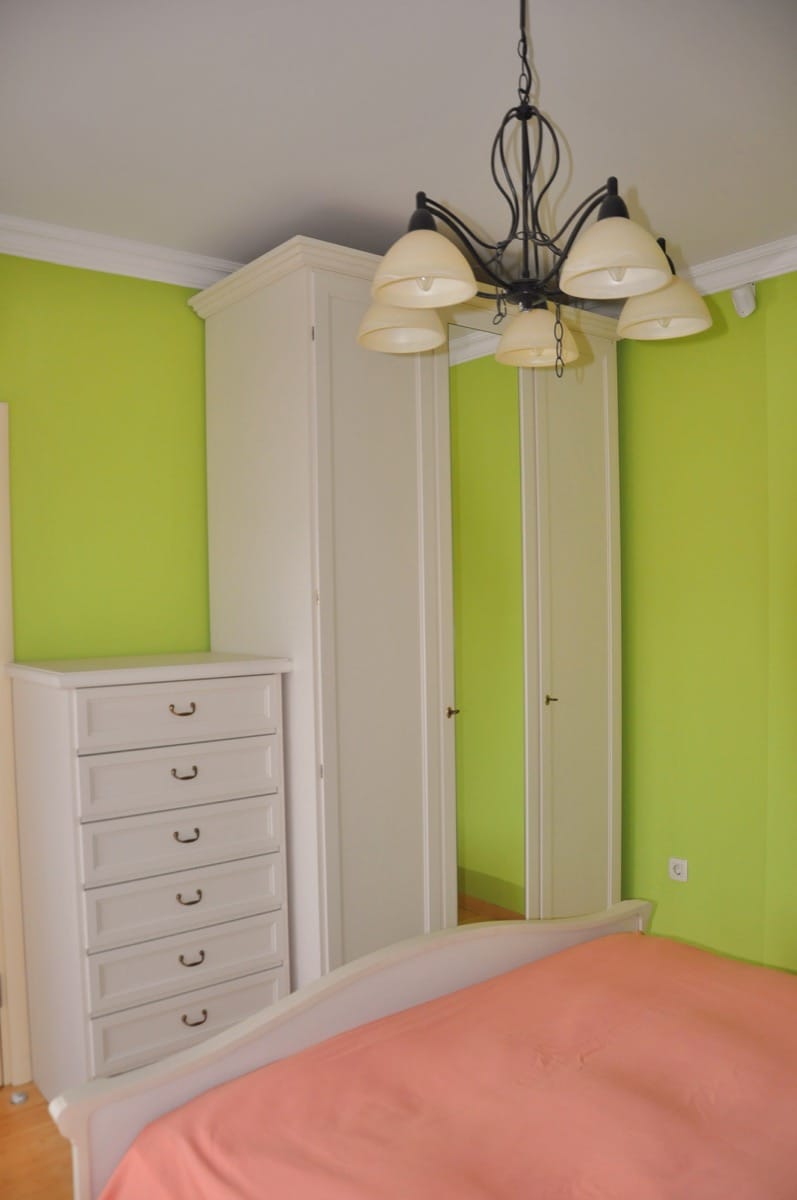 Bedroom in a villa in Đenovići, Montenegro: white furniture, a dresser, a wardrobe with a mirror, and a classic chandelier against the backdrop of the walls.
