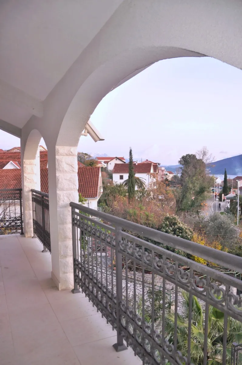Balcon couvert avec des arches en pierre et une rampe en métal donnant sur une ville et des montagnes.