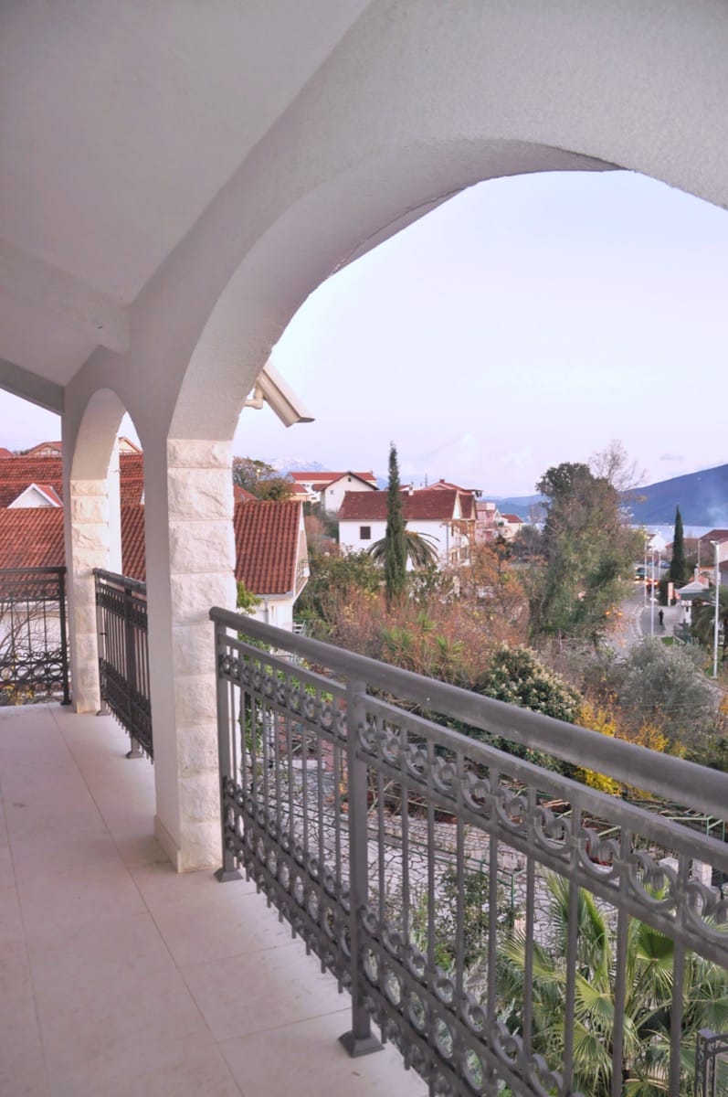Spacious balcony with stone arches and wrought-iron railing on a villa in Đenovići, Montenegro, overlooking the city.