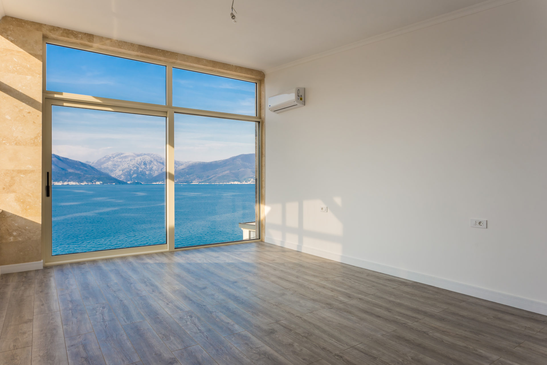 An empty modern room with a large window offering a view of the sea and mountains.