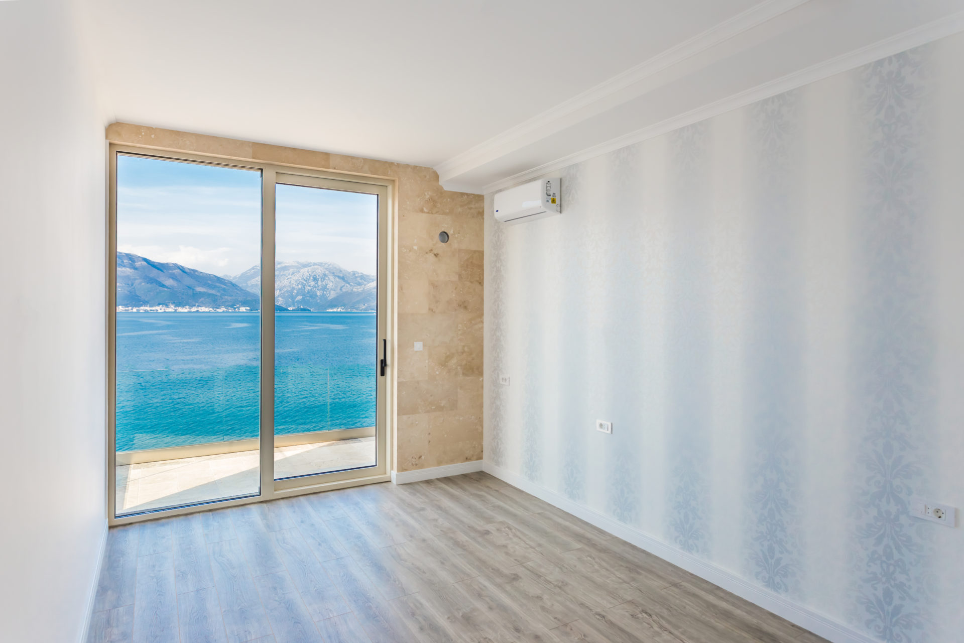 Empty room with a large window overlooking the sea and mountains.
