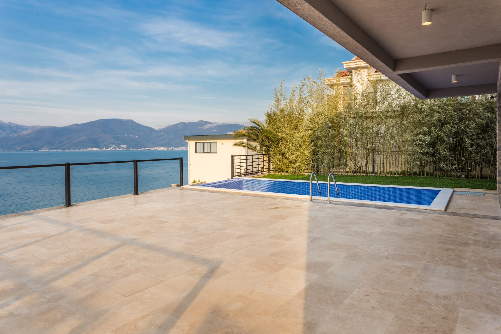 A stone terrace with a swimming pool, glass railing, and sea view.