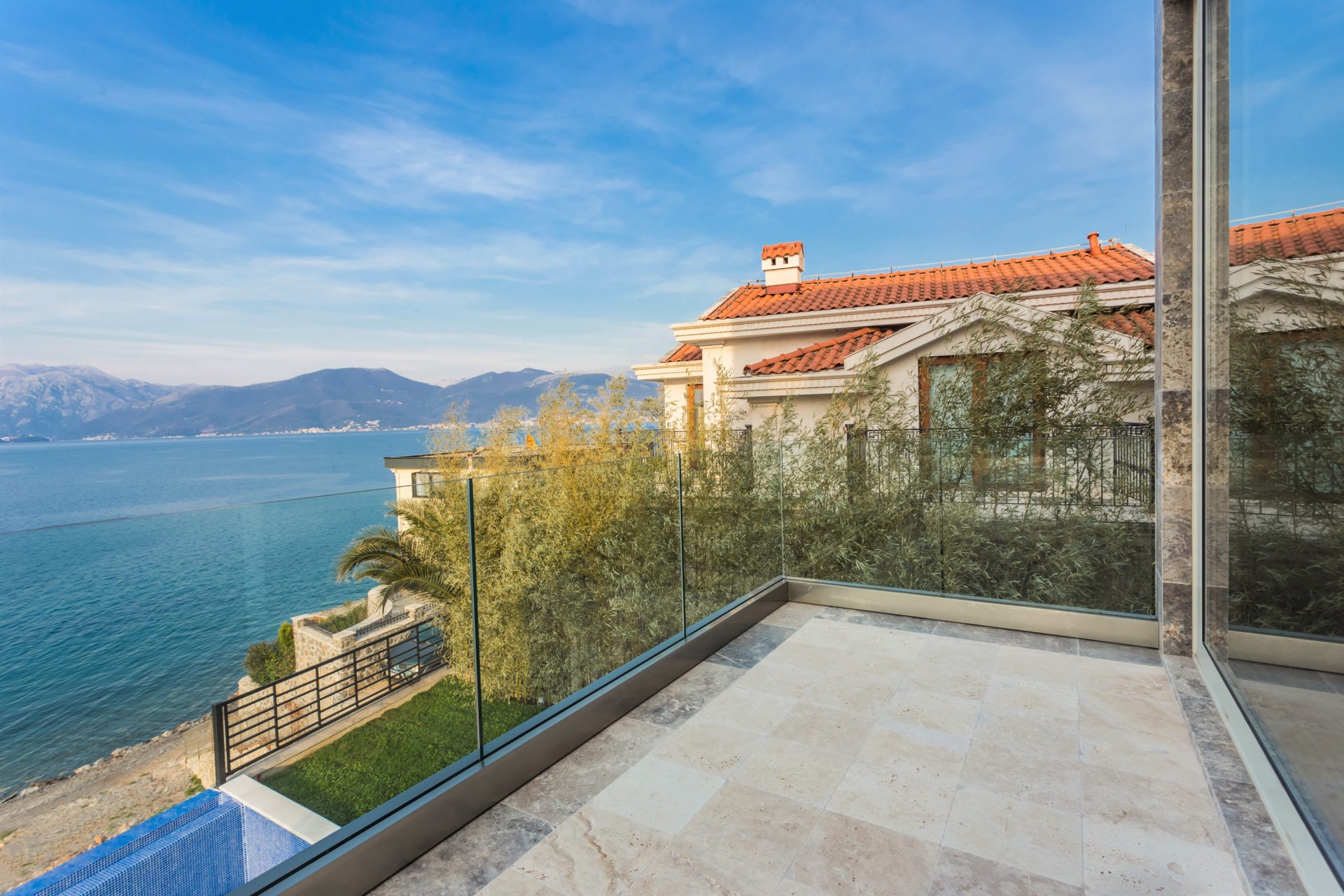 A balcony with glass railing overlooking the sea and mountains