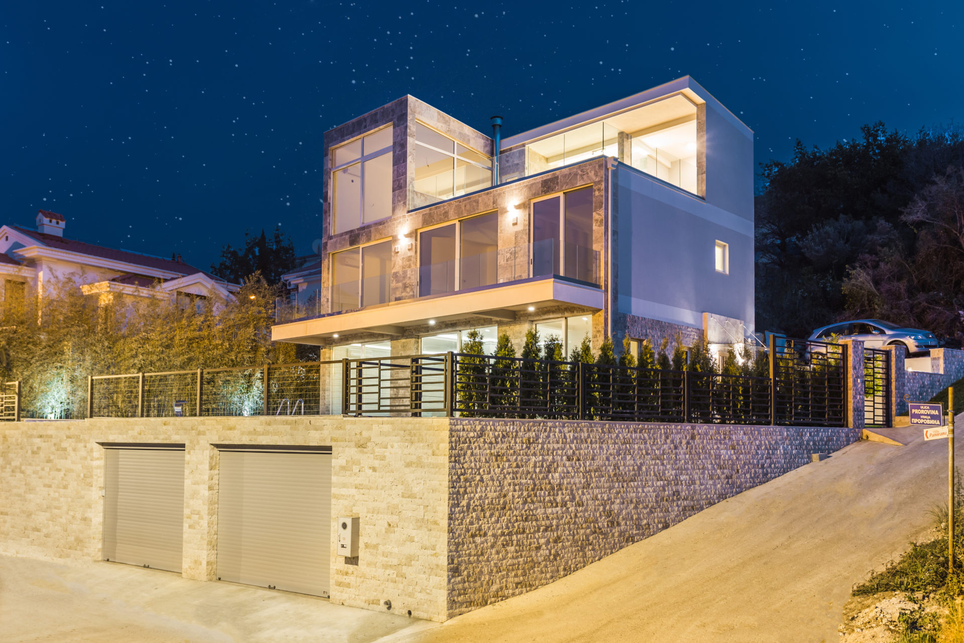 Modern three-story house with a garage and night lighting under a starry sky.