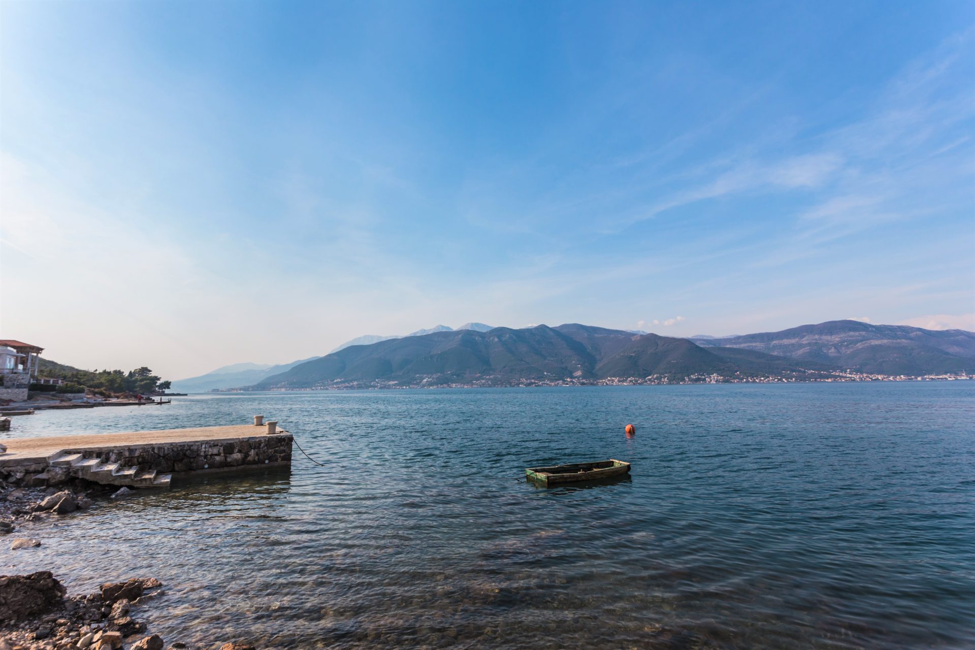 Scenic view of the sea, a small pier, and mountains in the background under a blue sky.