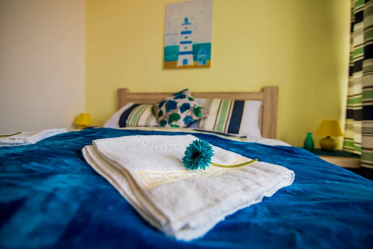 Ein gemütliches Schlafzimmer mit blauer Decke, weißen Handtüchern und einem Leuchtturmbild an der Wand.