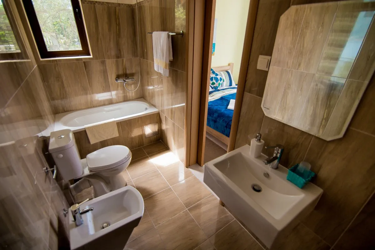 Ein kompaktes modernes Badezimmer mit Badewanne, Toilette, Bidet und Waschbecken sowie Blick in ein Schlafzimmer.