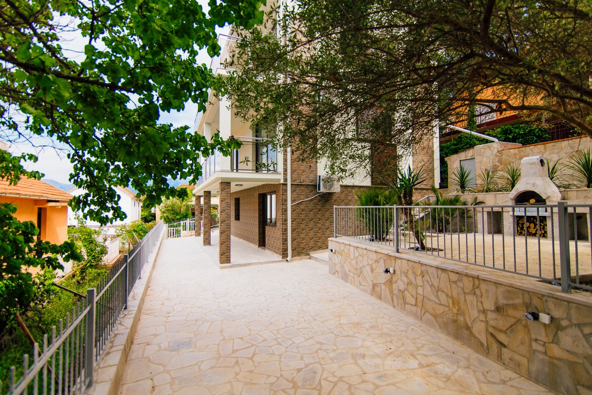 Karadağ, Krašići’de modern villa: taş kaplamalı teras, barbekü alanı ve evin ön cephesinin görünümü.