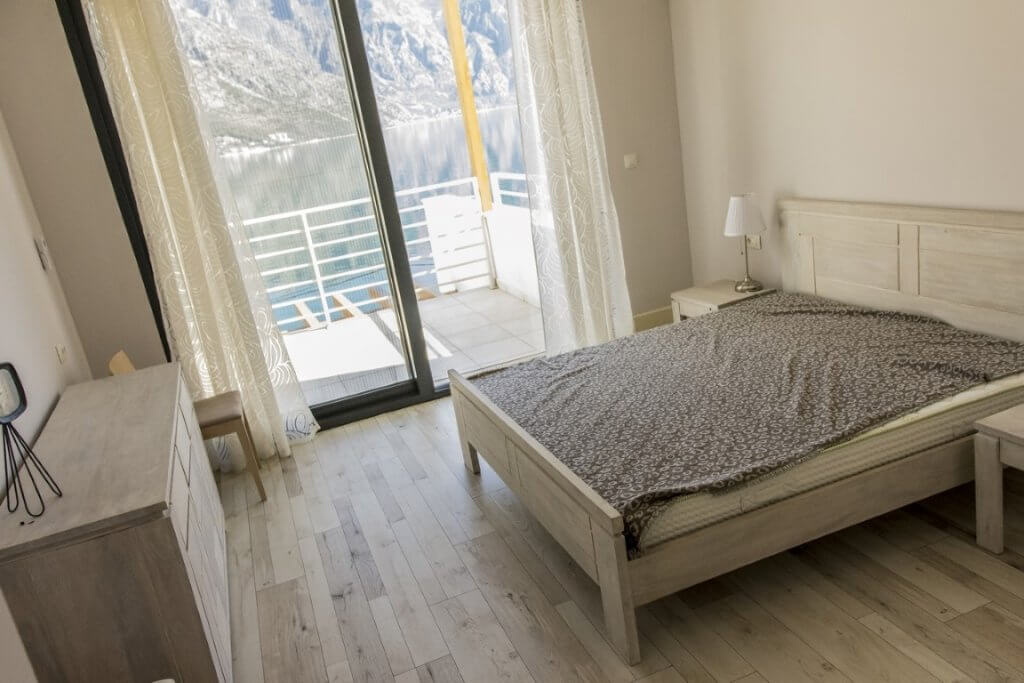 Schlafzimmer mit Doppelbett und Blick auf das Meer und die Berge in der Villa Stoliv, Montenegro, helles Interieur mit Panoramafenstern