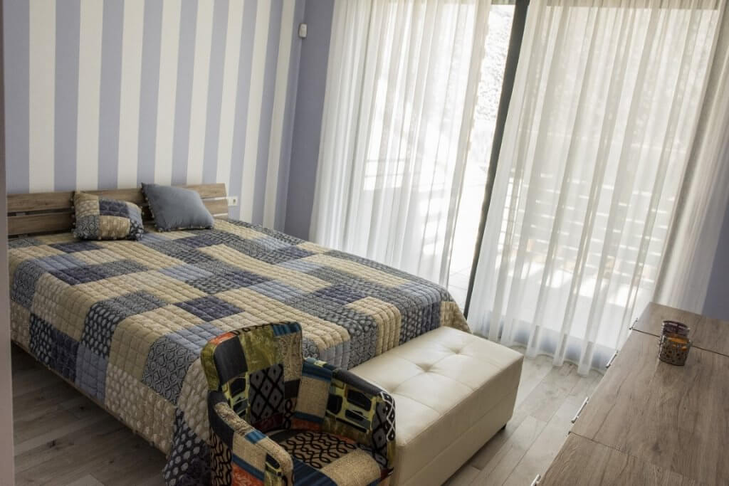 Gemütliches Schlafzimmer mit Doppelbett und Panoramafenster in einer Villa in Stoliv, Montenegro. Helles Interieur mit Möbeln.
