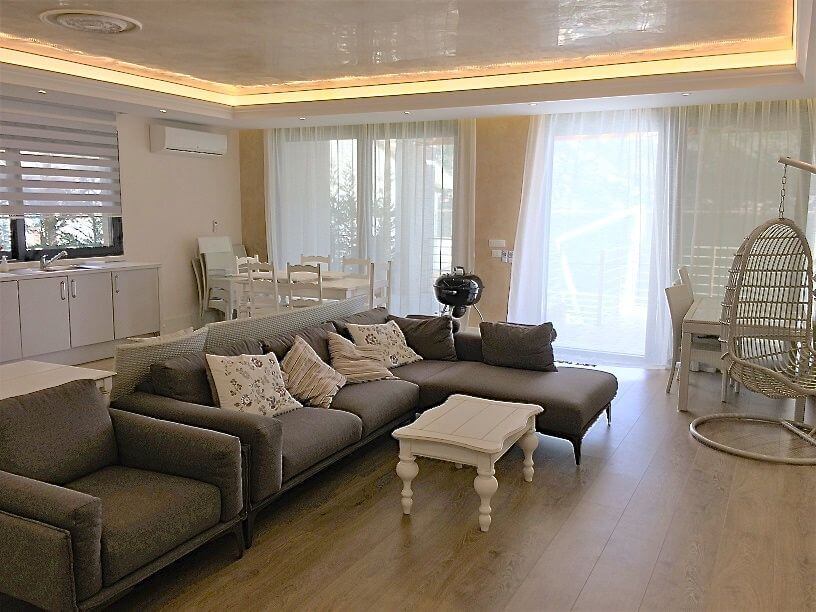 Wohnzimmer in einer Villa in Stoliv, Montenegro: graues Ecksofa, Kokon-Sessel, Essbereich und moderne Ausstattung.