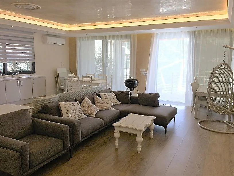 Salon w willi w Stolivie, Czarnogóra: szara narożna sofa, fotel kokon, jadalnia i nowoczesne wykończenie.