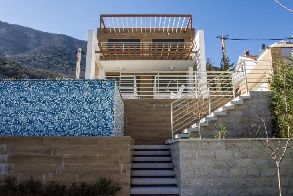 Moderne Villa in Stoliv, Montenegro: Fassade mit Terrasse, Pool und Steinverkleidung vor Bergkulisse.