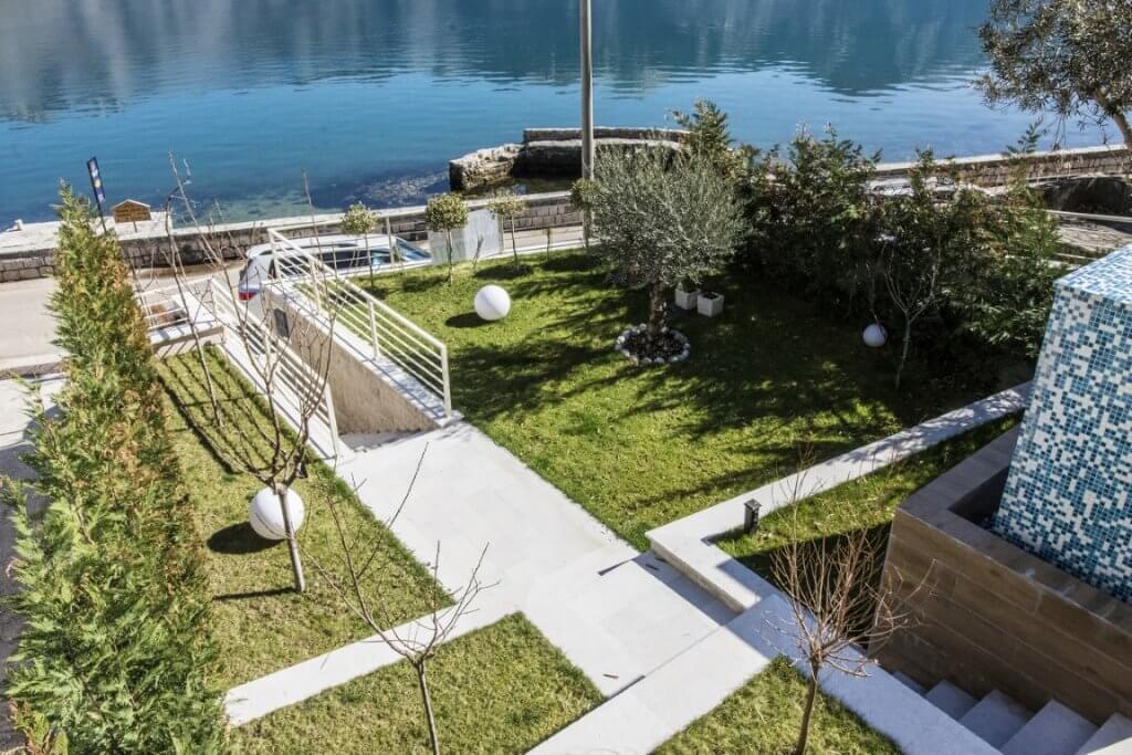 Gepflegter Garten mit Olivenbäumen und Meerblick bei der Villa in Stoliv, Montenegro, mit Zugang zur Uferpromenade.