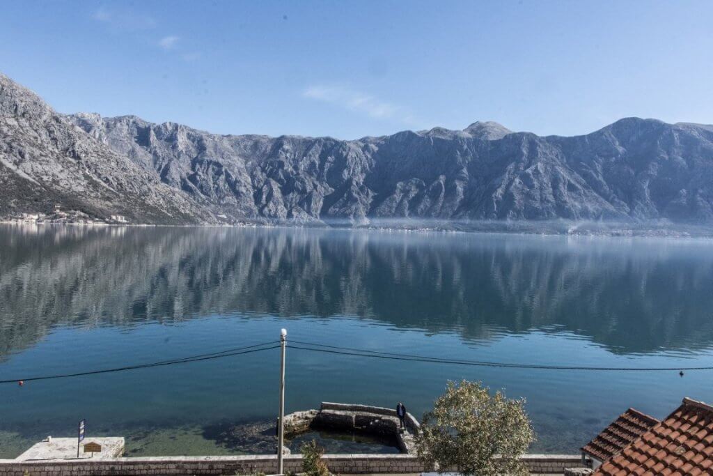 Panoramablick auf die Bucht von Kotor und die Berge von der Villa in Stoliv, Montenegro: Meereslandschaft mit Uferpromenade und Steg.