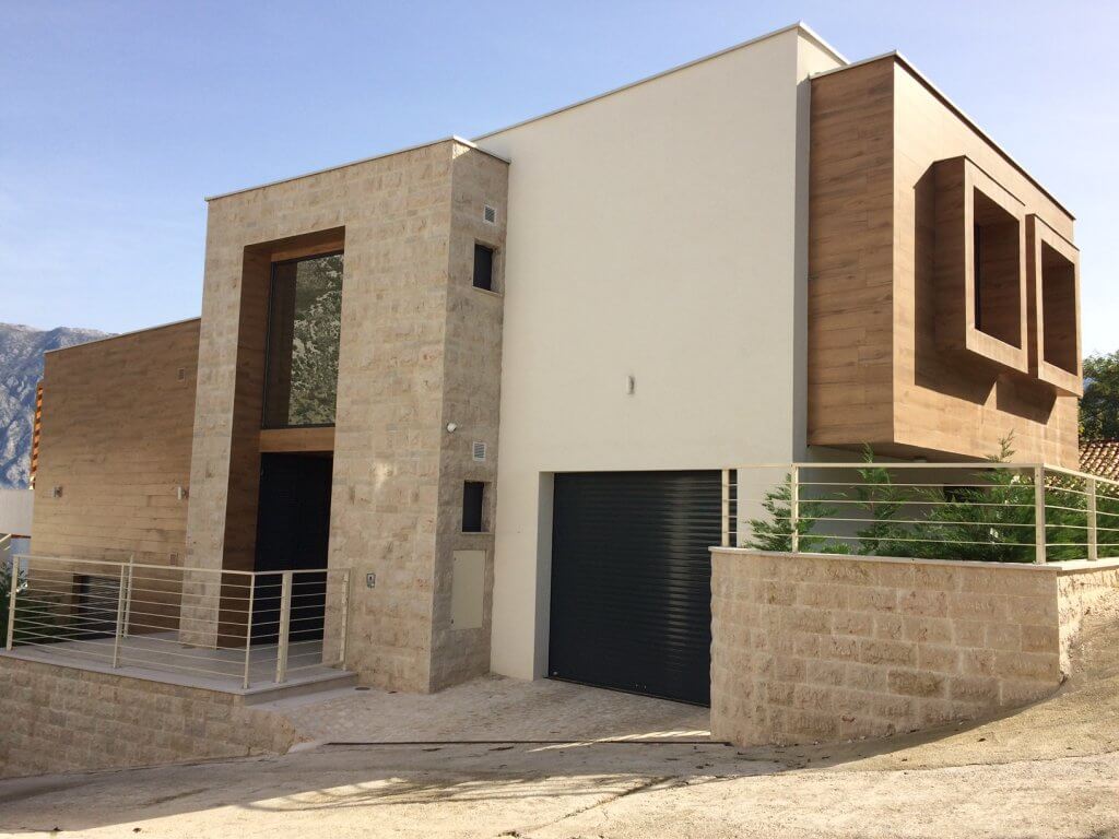 Moderne Villa in Stoliv, Montenegro: Fassade mit Stein- und Holzverkleidung, Garage und Panoramaverglasung.