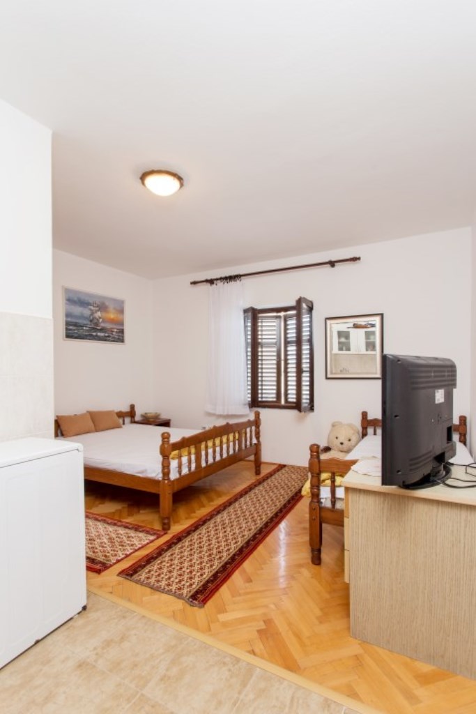 Schlafzimmer in einem Haus in Bijela, Montenegro: Holzbett, Parkett, Teppiche und ein Fenster mit Fensterläden in einem hellen Interieur.
