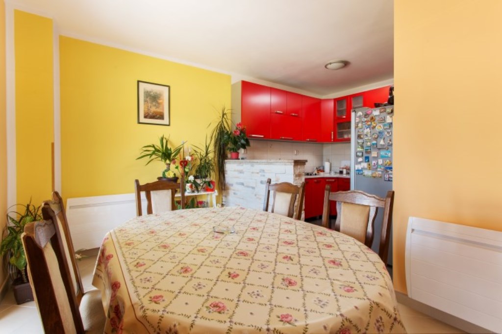 Küche und Esszimmer in einem Haus in Bijela, Montenegro: leuchtend gelbe Wände, rote Küchenmöbel und ein Essbereich mit Tisch.