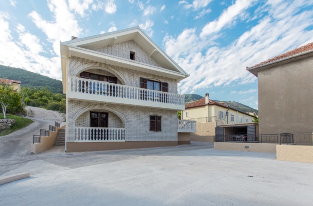 Zweistöckiges Haus mit Ziegelverkleidung, Bogenbalkonen und Parkplatz in der Stadt Bijela, Montenegro.