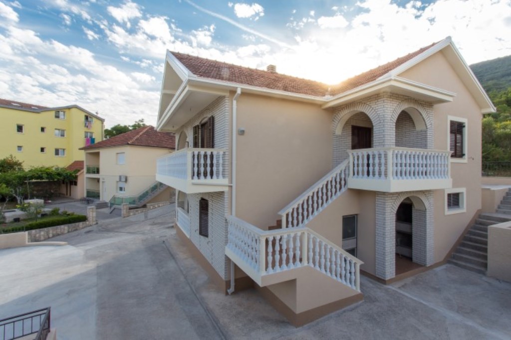 Zweistöckiges Haus mit Terrassen und Außentreppe in der Stadt Bijela, Montenegro, Blick auf die Fassade und das angrenzende Grundstück.