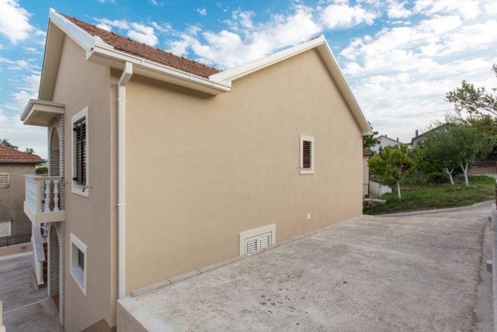 Fassade eines zweistöckigen Hauses in Bijela, Montenegro: beige Wände, Ziegeldach, Balkon mit Balustrade und Grundstücksbereich.