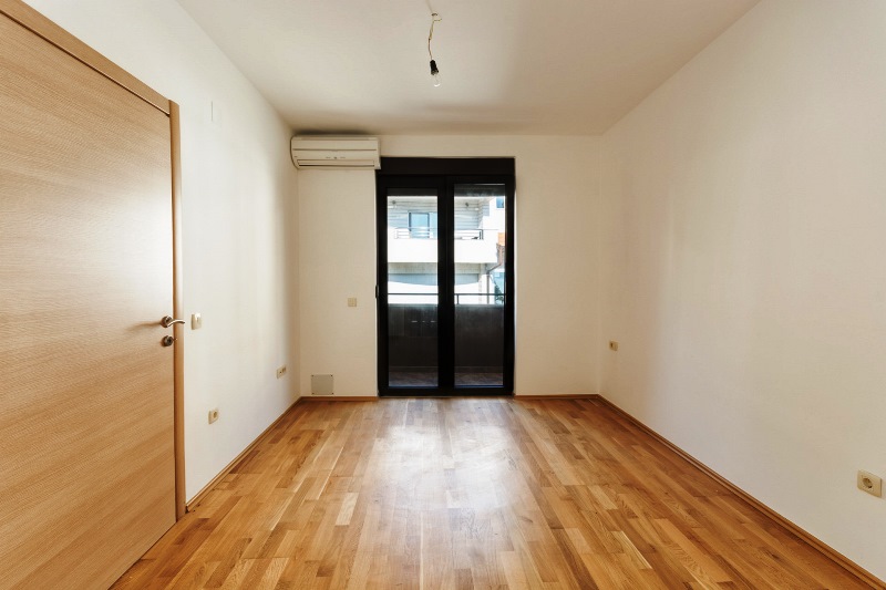 Svetla spavaća soba sa parketom i izlazom na balkon u stanu, grad Orahovac, Crna Gora.