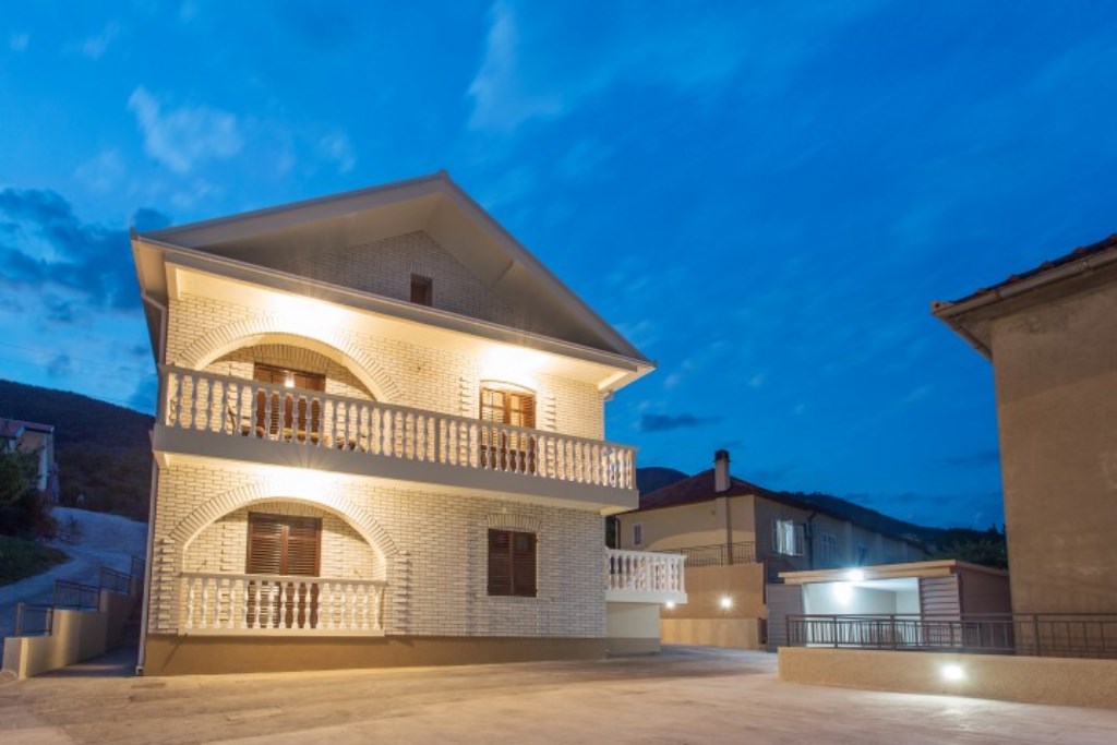 Zweistöckiges Haus mit Ziegelverkleidung, Bogenbalkonen und Beleuchtung in Bijela, Montenegro.