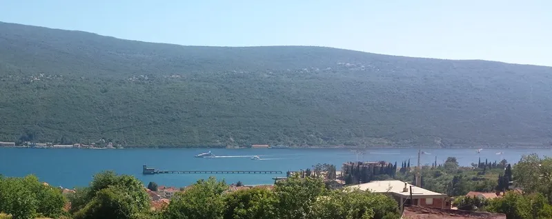 Blick von einem Hügel auf eine Bucht, einen bewaldeten Berg und Boote auf dem Wasser.