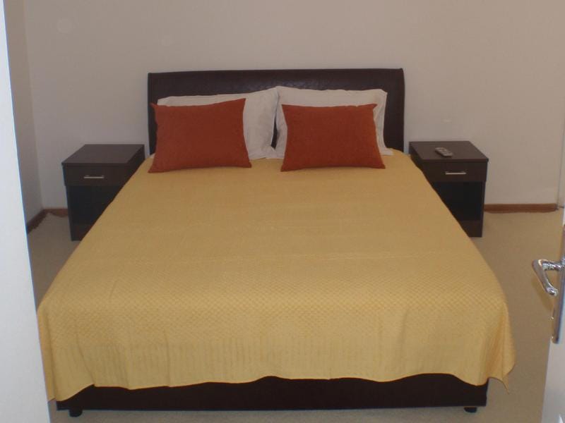 Bedroom in a house in Baošići, Montenegro: a double bed with a yellow bedspread and dark bedside tables.