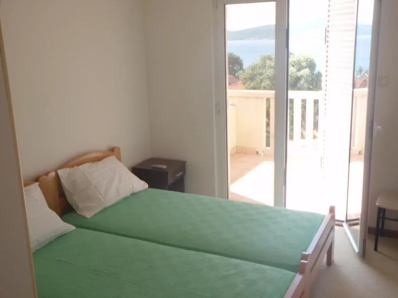 Spavaća soba sa dva kreveta i izlazom na balkon s pogledom na more u kući, Baošići, Crna Gora.