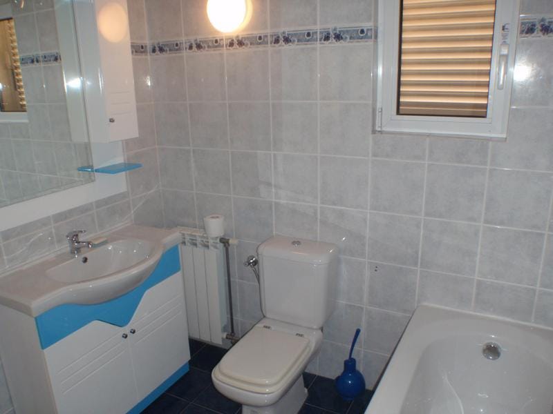 Bright bathroom in a house in Baošići, Montenegro: tiles, plumbing fixtures, vanity with sink, and a window with blinds.