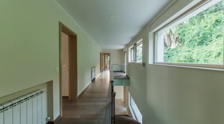 Ein moderner langer Flur mit Holzboden, Wänden, Türen, Fenstern und einem Treppengeländer.