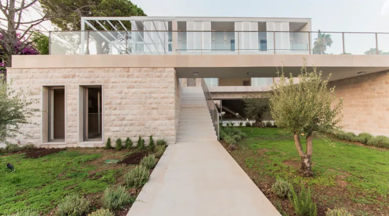 Außenbereich einer modernen Villa mit Steinfassade, zentraler Treppe, Terrasse und gepflegtem Garten.