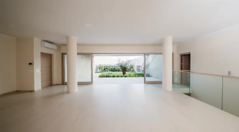 Helles minimalistisches Wohnzimmer mit zwei Säulen und Glasgeländer mit Blick auf die Terrasse.