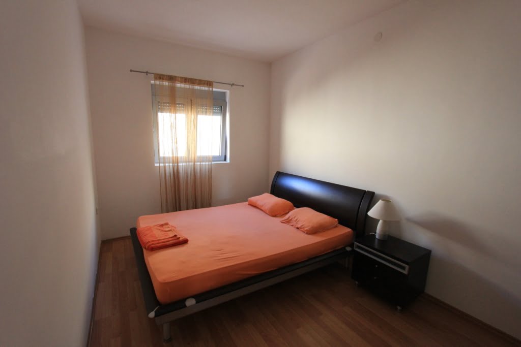 Sypialnia z łóżkiem dwuosobowym i stolikiem nocnym w mini-hotelu, Orahovac, Czarnogóra. Jasne wykończenie, laminat.
