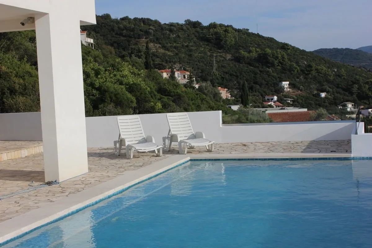 Pool am Haus in Dobra Voda, Montenegro: Terrasse mit Liegestühlen, Steinverkleidung und Panoramablick auf die Berge.