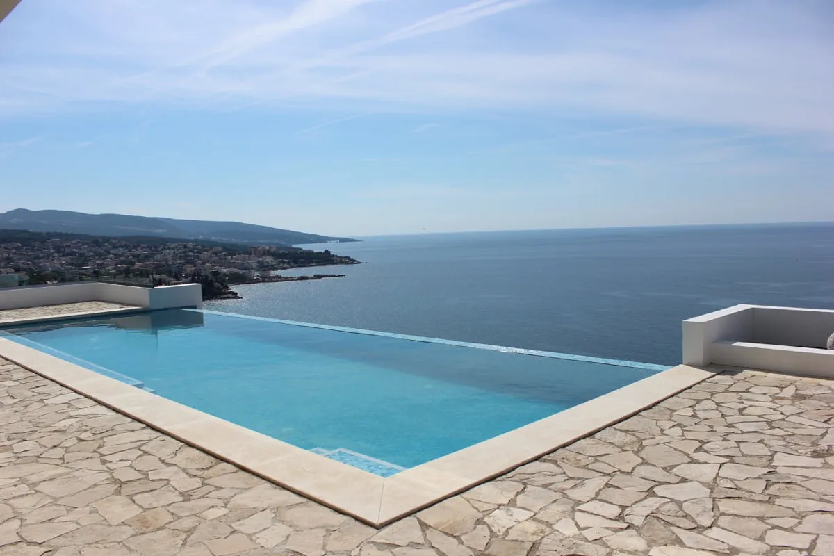 Infinity-Pool mit Panoramablick auf das Meer und die Küste in einem Haus in Dobri Vode, Montenegro. Terrasse mit Steinverkleidung.