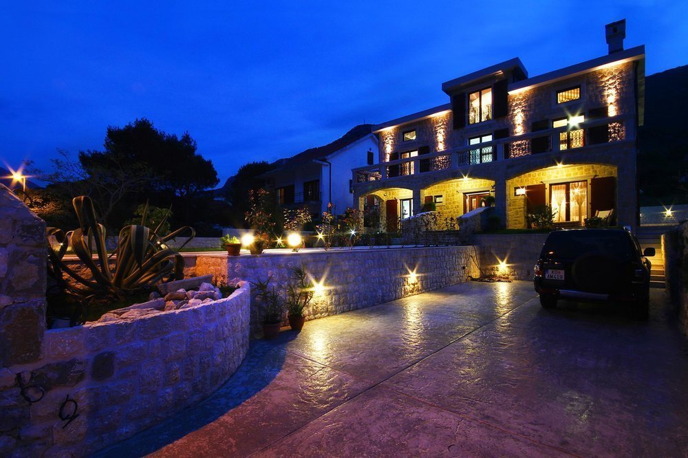 Karadağ, Prčanj’da gece cephe aydınlatmalı, teraslı ve evin yanında otoparkı bulunan iki katlı taş villa.
