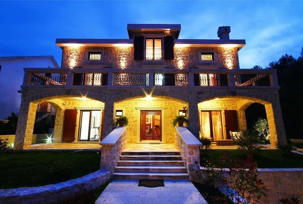 Karadağ, Prčanj'da aydınlatmalı ve teraslı üç katlı taş villa: akşam saatlerinde cephe görünümü.