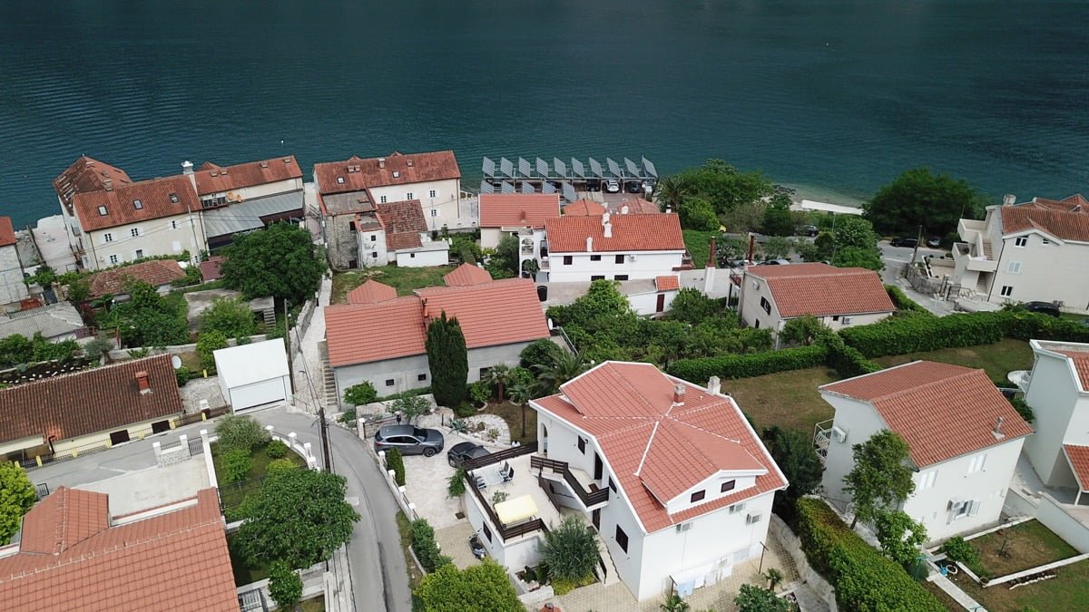Karadağ, Prčanj’daki villanın havadan görünümü: Kotor Körfezi kıyısında kırmızı kiremitli beyaz evler ve yeşil alan.