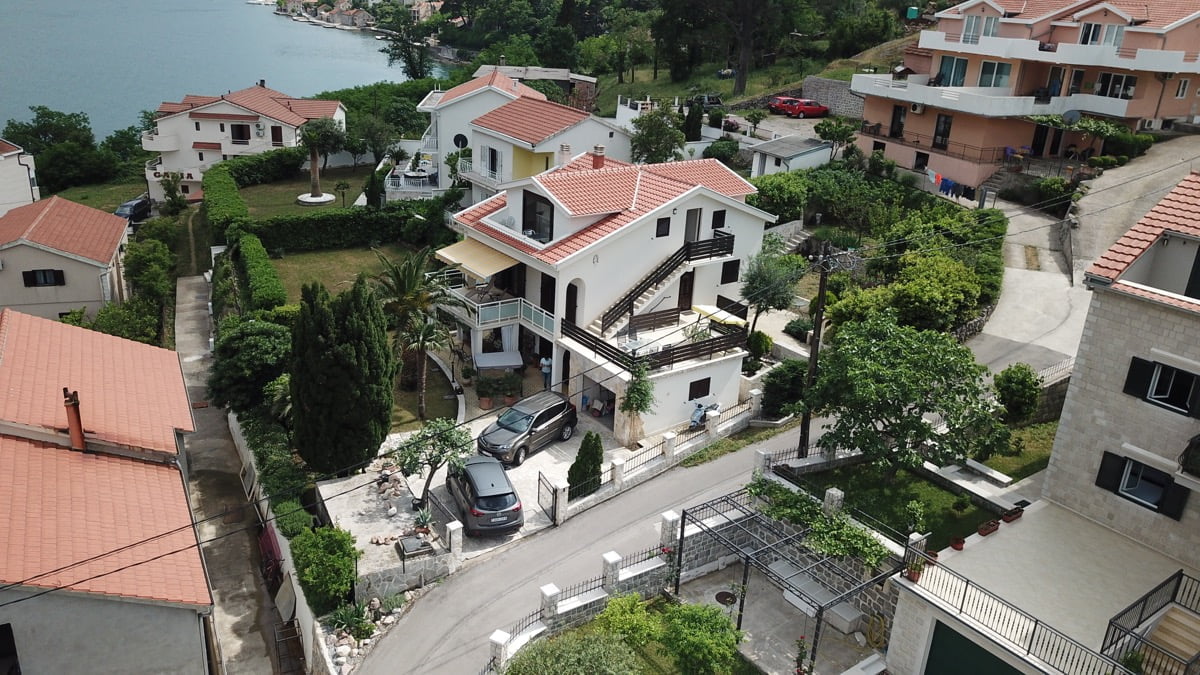 Karadağ, Prčanj’da üç katlı villa: terasları, otoparkı ve Kotor Körfezi kıyısındaki bahçesiyle evin yukarıdan görünümü.