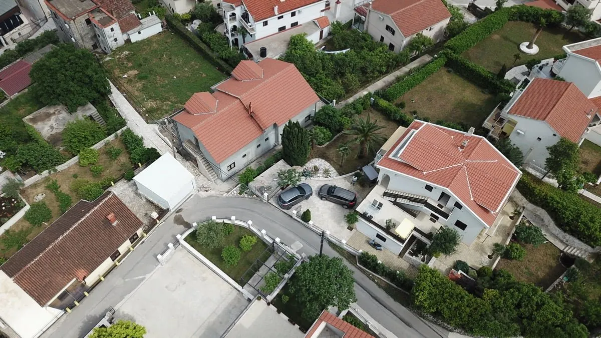 Luftaufnahme einer Villa in Prčanj, Montenegro: ein Privathaus mit Ziegeldach, Parkplatz und grünem Grundstück.