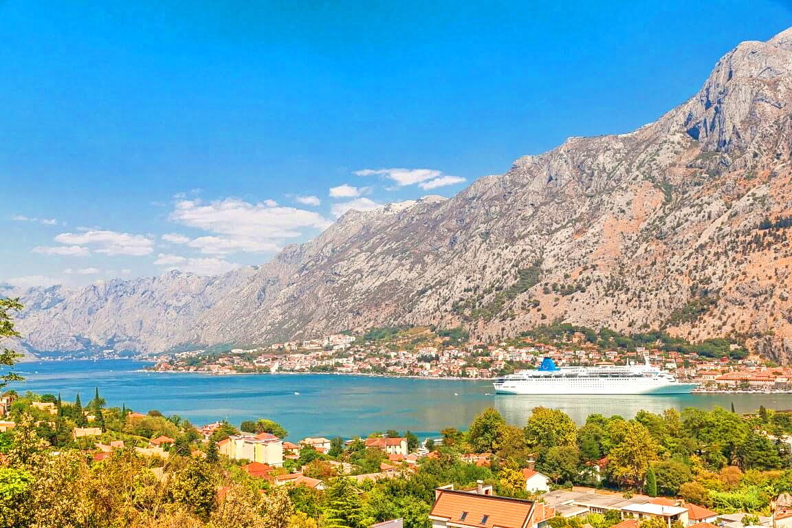 Panoramablick auf die Bucht von Kotor, die Berge und ein Kreuzfahrtschiff aus einer Wohnung in Kotor, Montenegro.