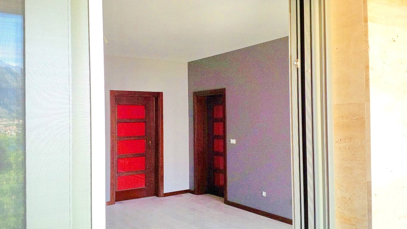 Innenraum des Wohnzimmers in einer Wohnung, Kotor, Montenegro: helle Wände, dunkle Innentüren und Blick auf die Berge aus dem Fenster.